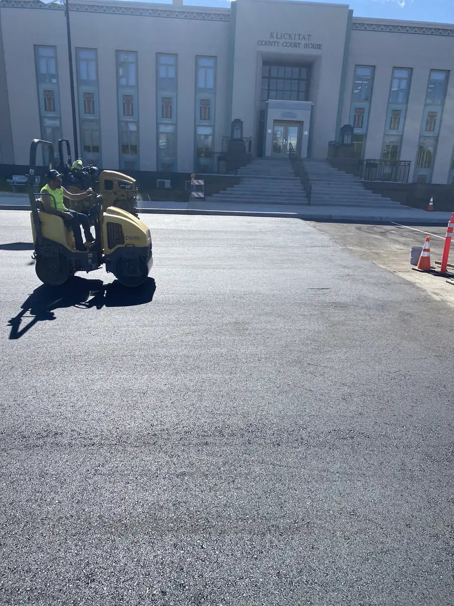 Crew member working on fresh asphalt in front of a stone building