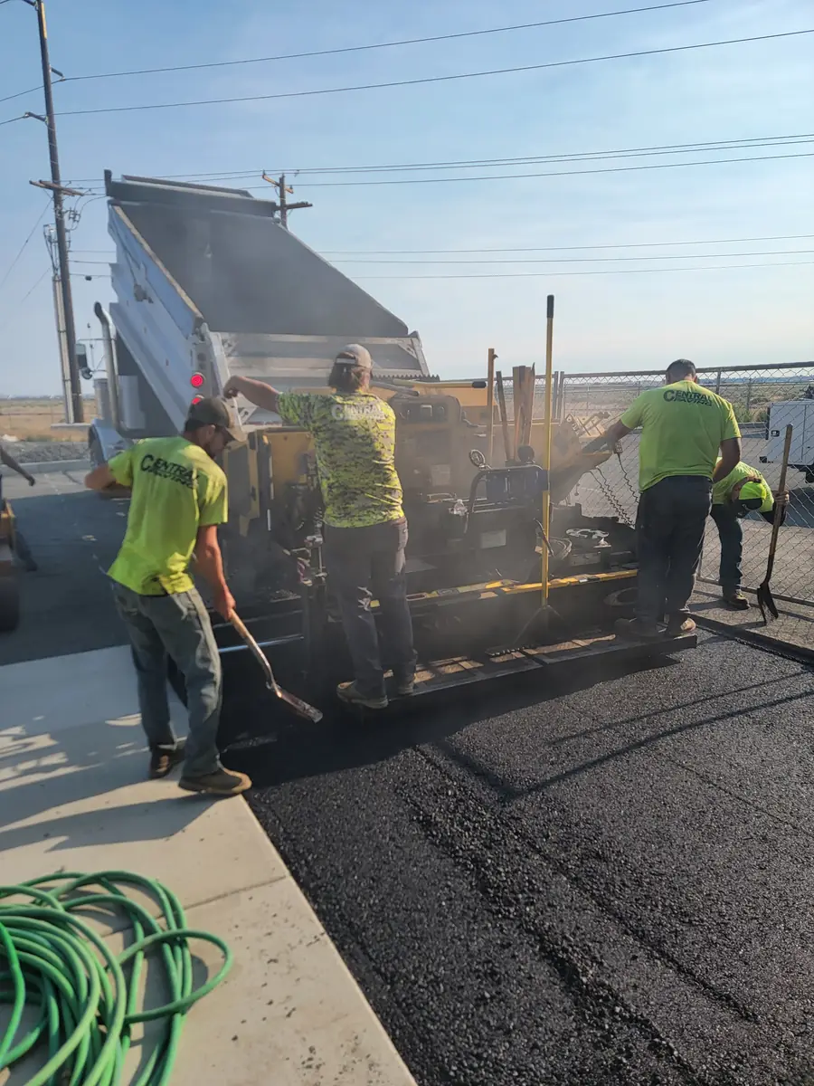 Crew working around a paver and dump truck on a street