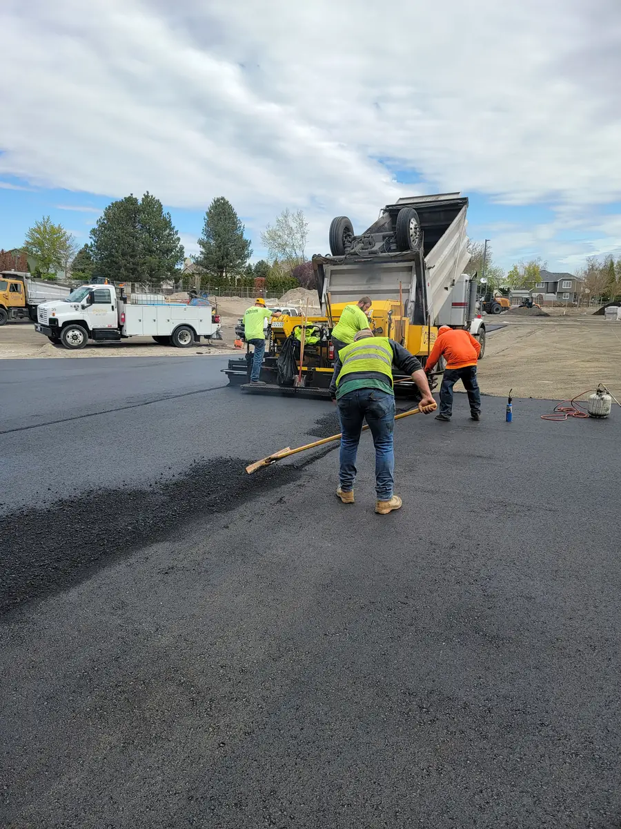 Crew raking fresh asphalt behind a paver on a lot