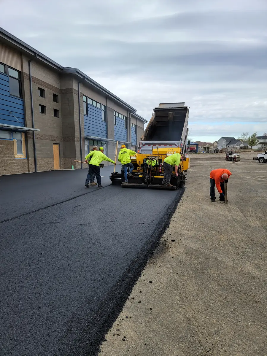 Paver laying asphalt beside a school-style building