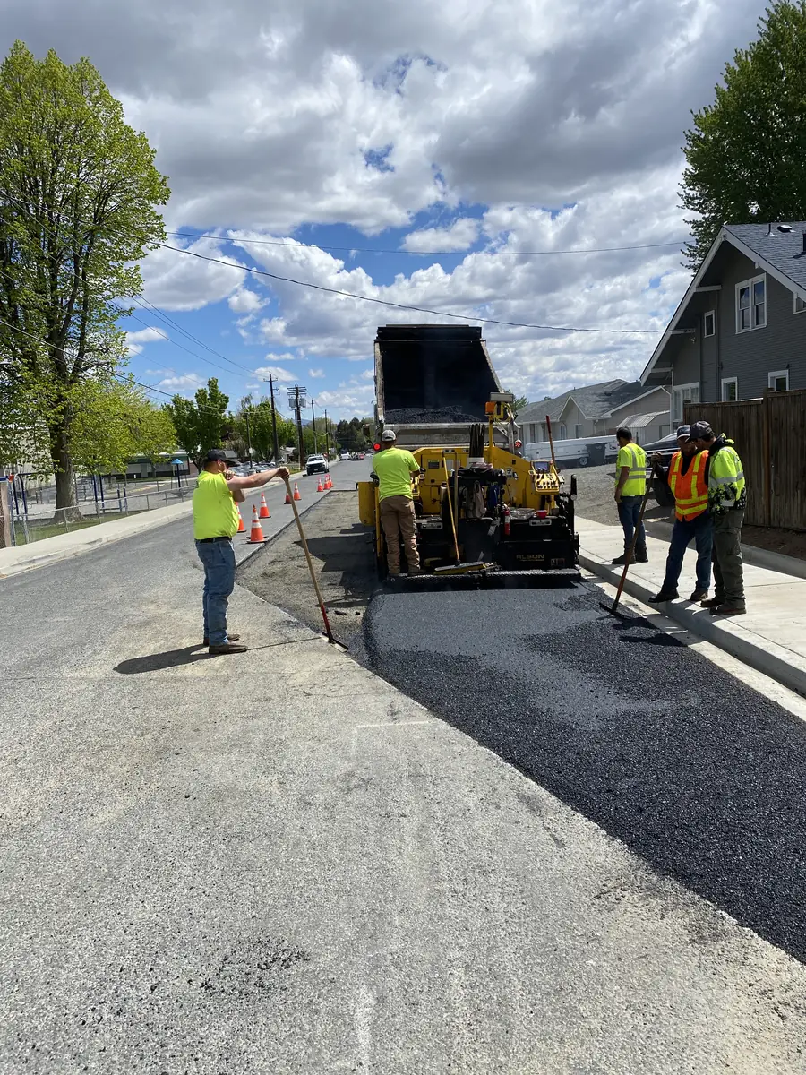 Paver laying asphalt on a street with crew members nearby