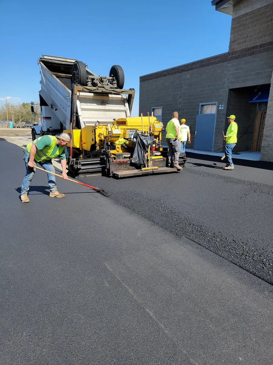 Paver and crew laying asphalt beside a commercial building