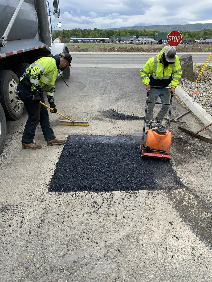 Crew member using a plate compactor on an asphalt patch