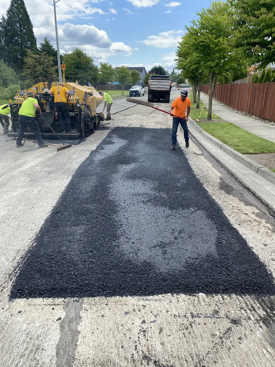 Freshly patched section of street with a crew and truck behind it