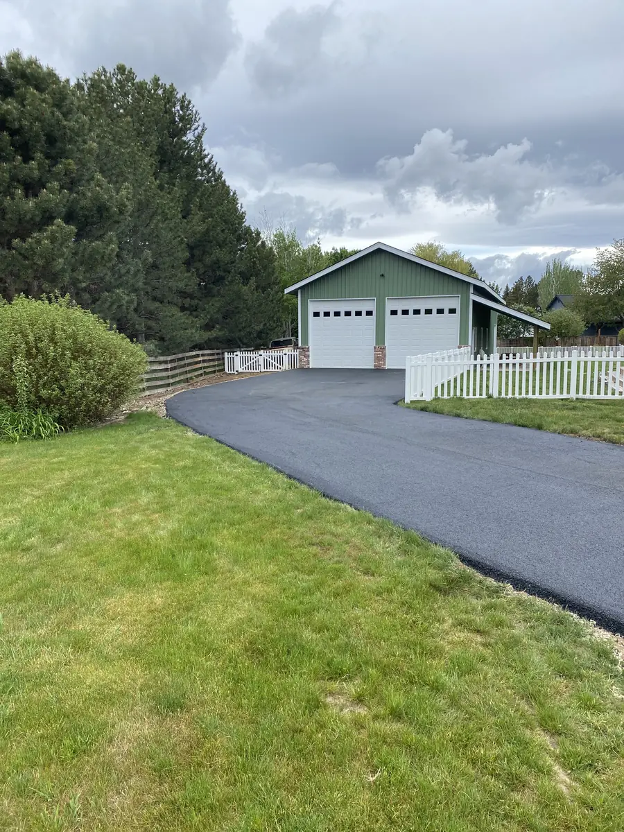 New asphalt driveway leading to a garage beside a lawn