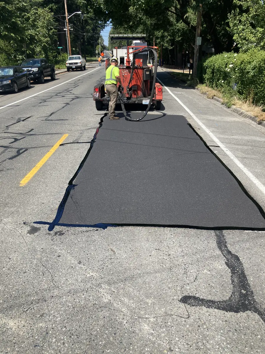Newly patched rectangle of asphalt in a parking lot with a sealed crack beside it