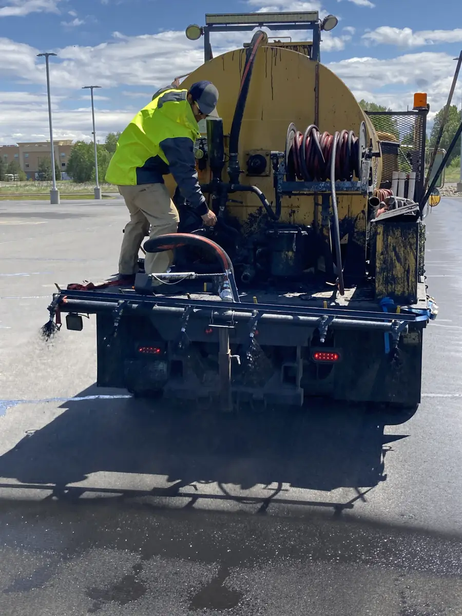 Crew member operating a sealcoat spray truck on pavement