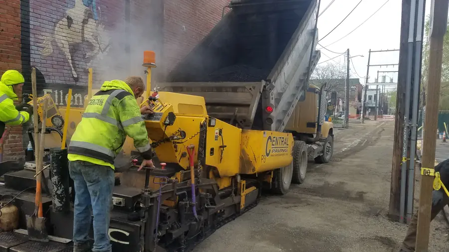 Central Paving crew working at the back of a paver as a dump truck feeds it hot asphalt