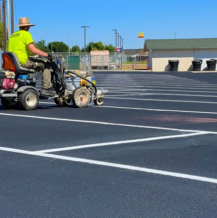 Central Paving crew member operating a ride-on line striping machine in a commercial parking lot
