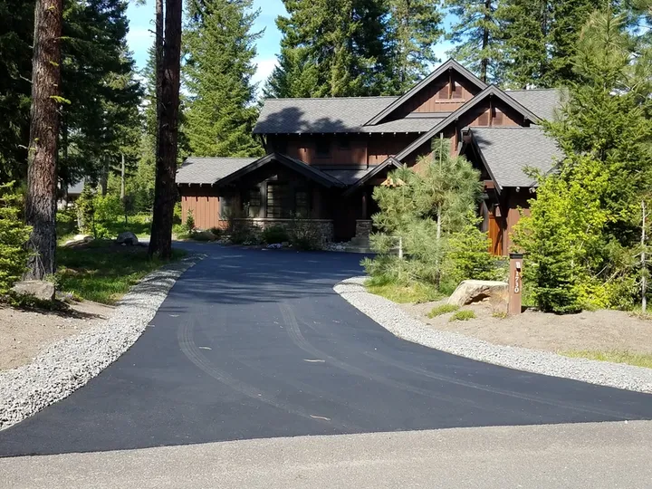 Newly sealcoated curving driveway leading to a log-style home surrounded by pine trees