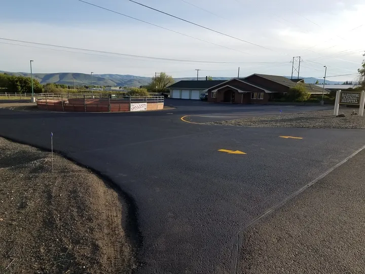 Freshly sealcoated rural parking area with yellow markings and a gravel shoulder
