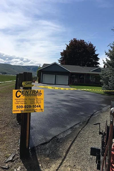 Freshly sealcoated driveway with a Central Paving job sign in front of a home